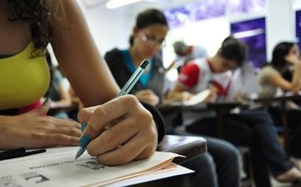 Estudantes universitários em sala de aula com jovem mulher escrevendo em caderno em primeiro plano