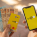 Mãos segurando cartão amarelo Will Bank Mastercard, notas de R$50 e R$100, e celular com app Will Bank aberto