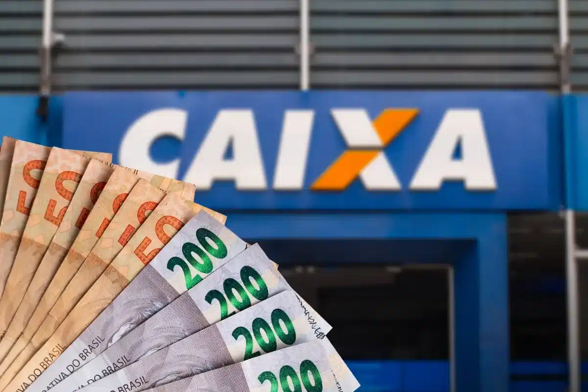 Notas de 200 reais sendo seguradas em frente a uma agência da Caixa Econômica Federal, com referência ao Saque Calamidade do FGTS de R$ 6.220.