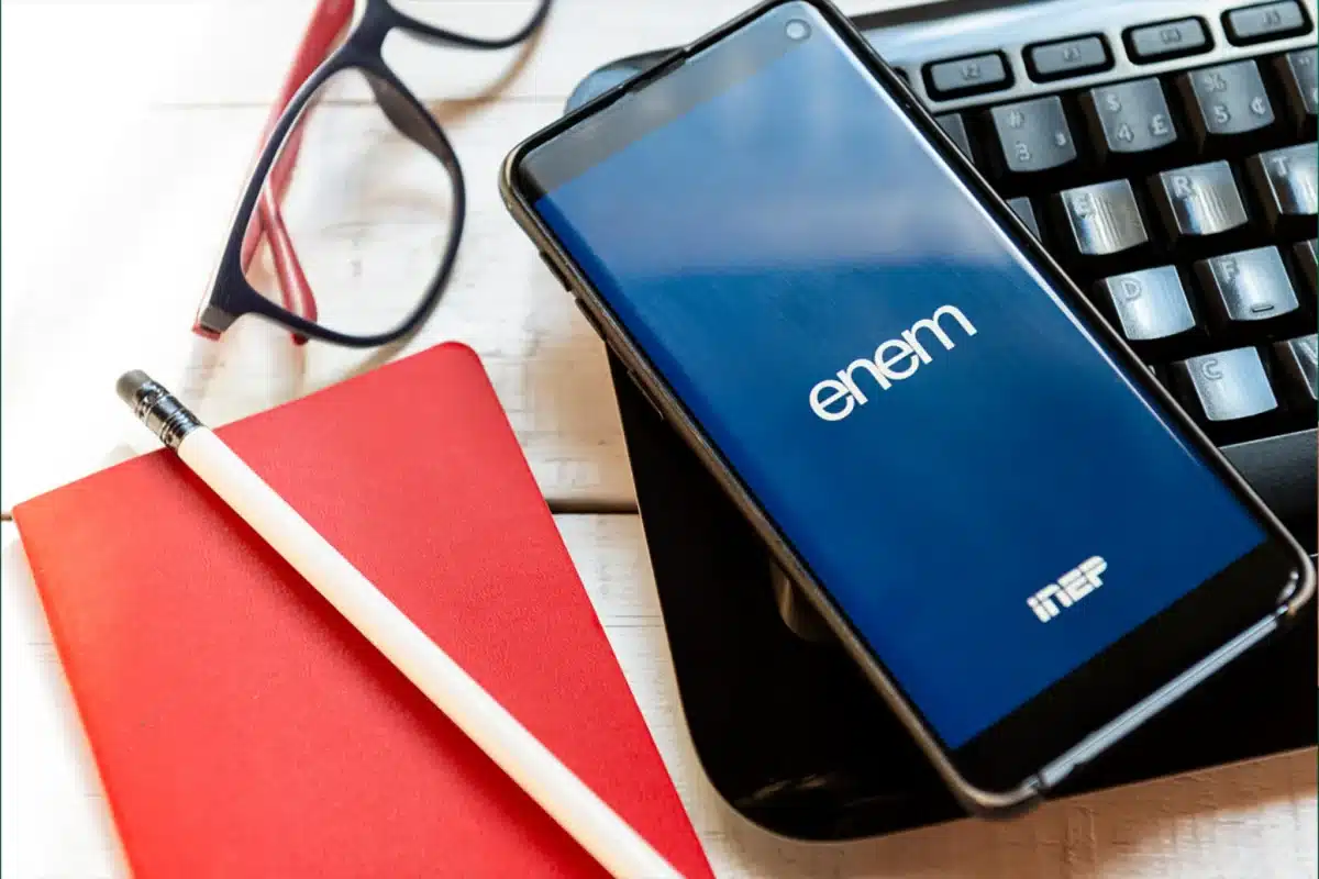 Celular exibindo a tela do Enem sobre mesa com materiais de estudo, representando preparação para vestibulares em 2026. 