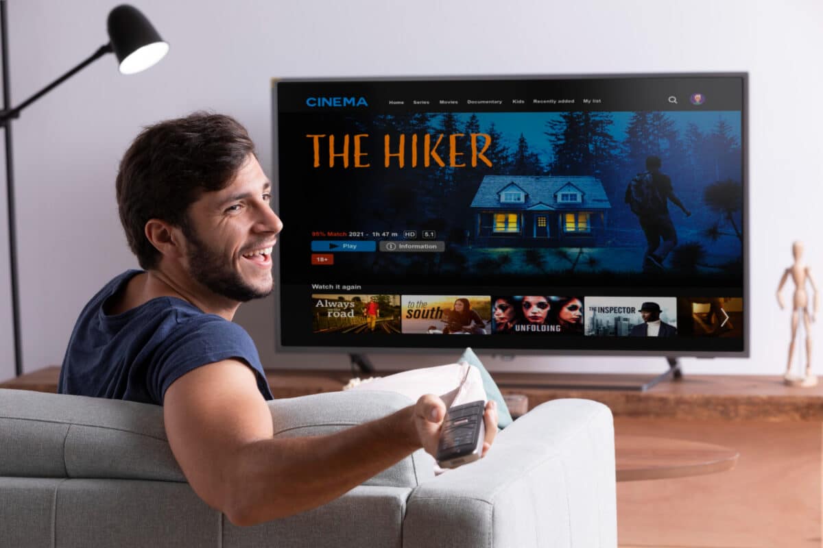 Homem sorridente sentado no sofá assistindo filme em smart TV de tela grande na sala de estar