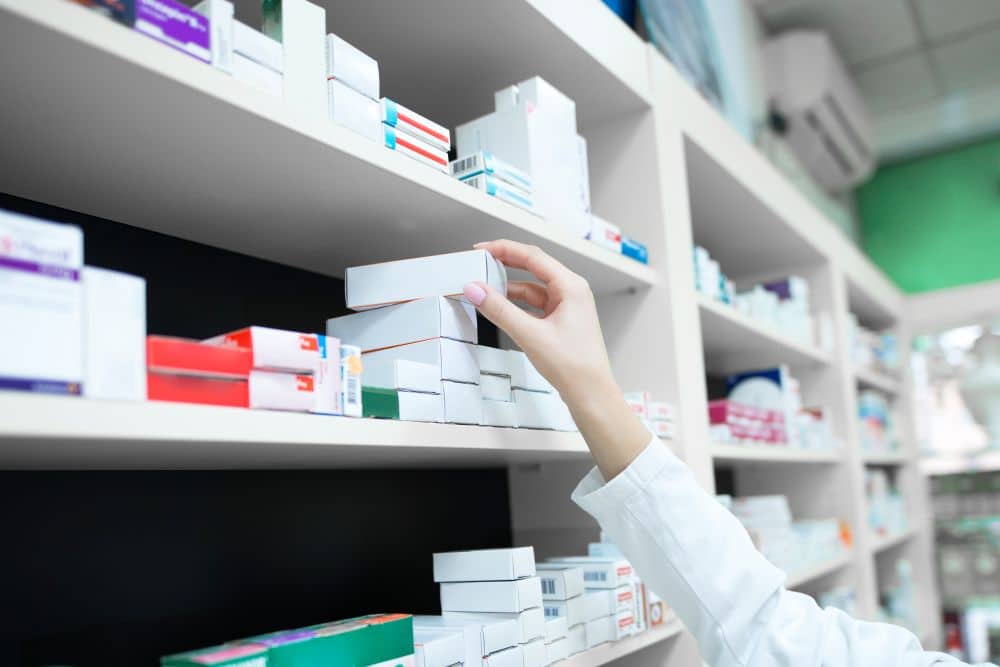 Mão feminina colocando uma caixa de medicamentos em uma prateleira da farmácia.