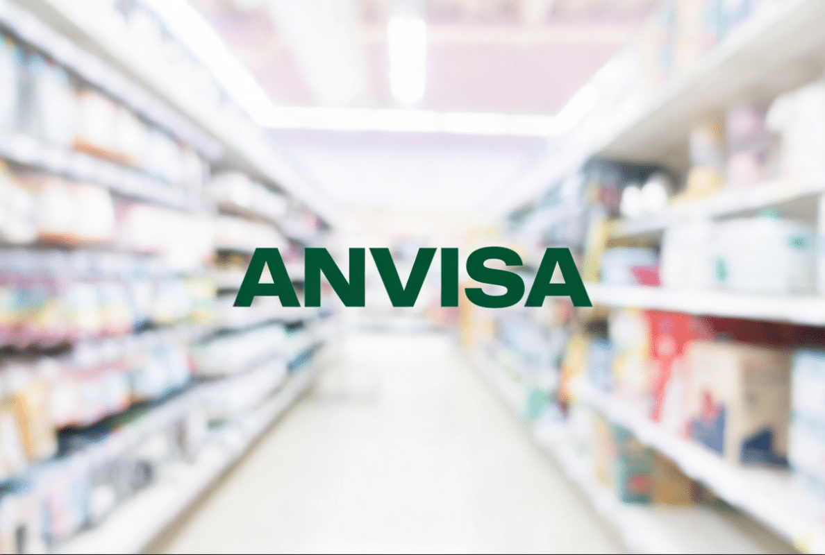 Nome "ANVISA" em corredor de farmácia com prateleiras de medicamentos.