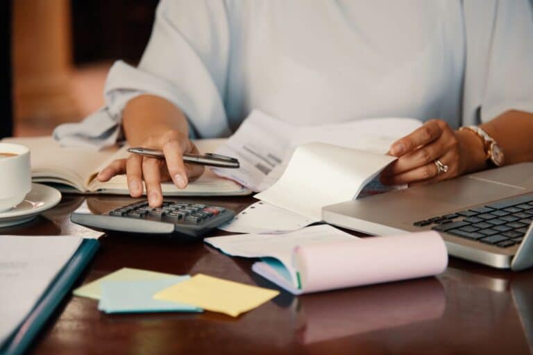 Mulher organiza finanças com calculadora e documentos.