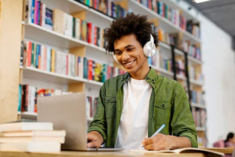 Estudante usando notebook e fones de ouvido enquanto aprende idiomas em uma biblioteca.