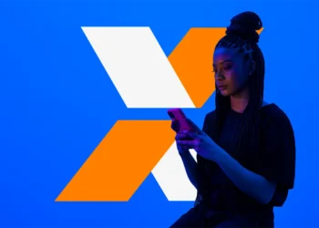 Jovem mulher com tranças consultando o celular sobre fundo azul com letra X em laranja e branco