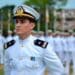 Oficial da Marinha de uniforme branco e quepe em destaque diante de formação militar enfileirada ao fundo em pátio externo