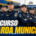 Oito guardas municipais fardados de azul-marinho com coletes e bonés, braços cruzados, em frente à base operacional