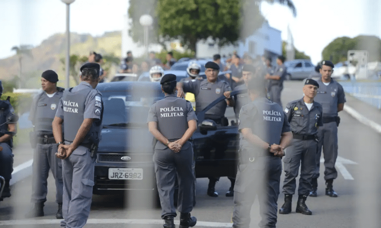 Policiais militares uniformizados em formação ao lado de viaturas durante operação ao ar livre