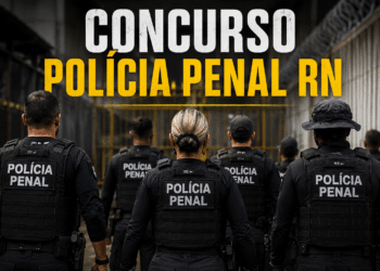 Agentes da Polícia Penal de costas com coletes táticos pretos diante de portão amarelo de unidade prisional.