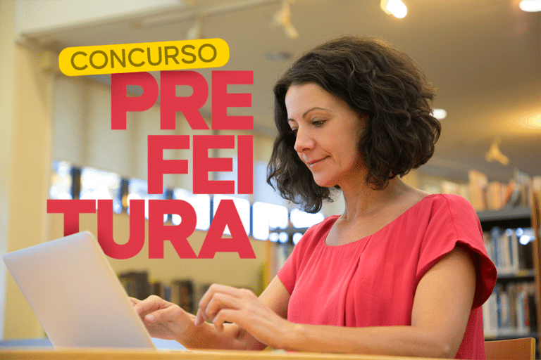 Mulher de cabelos cacheados escuros usando blusa coral digita em notebook branco em ambiente de biblioteca