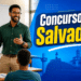 Professor negro com óculos e camisa verde leciona para alunos com palavras motivacionais no quadro e arte de Salvador ao fundo
