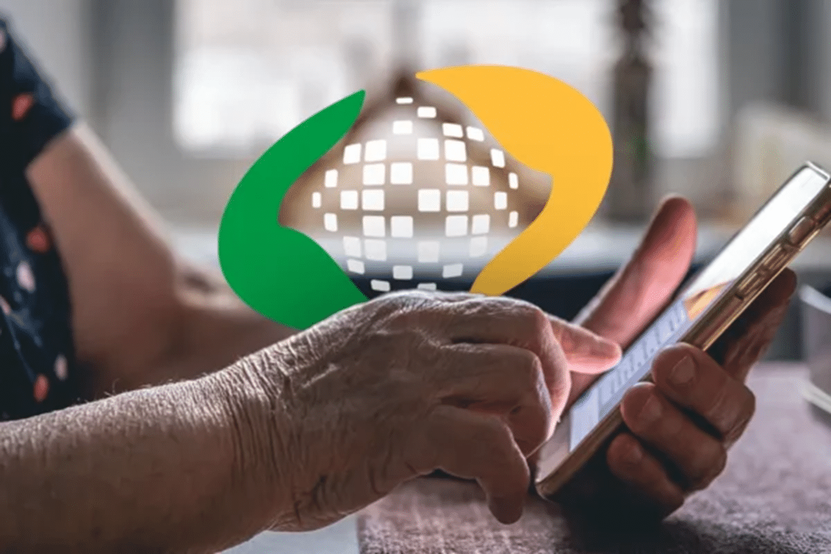 Mãos de idosa operam smartphone com ícone digital da Previdência Social ao fundo