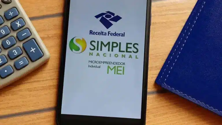 Tela de celular exibe logos da Receita Federal e do Simples Nacional para Microempreendedor Individual ao lado de calculadora cinza sobre mesa de madeira.