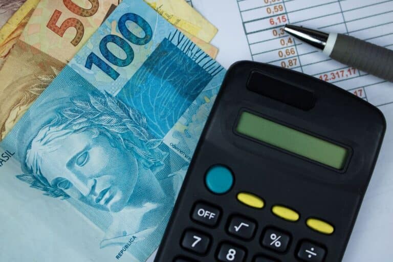 Cédulas de R$ 50 e R$ 100 ao lado de calculadora preta sobre planilha financeira, em referência à renegociação de dívidas pelo Novo Desenrola Brasil