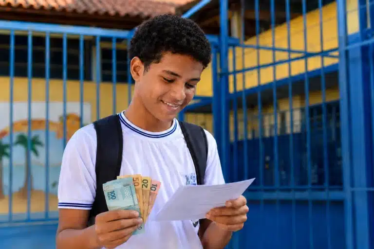 Estudante da rede pública segurando documentos do Enem 2026 e cédulas de dinheiro, representando a gratuidade do exame e o bônus de R$ 200.