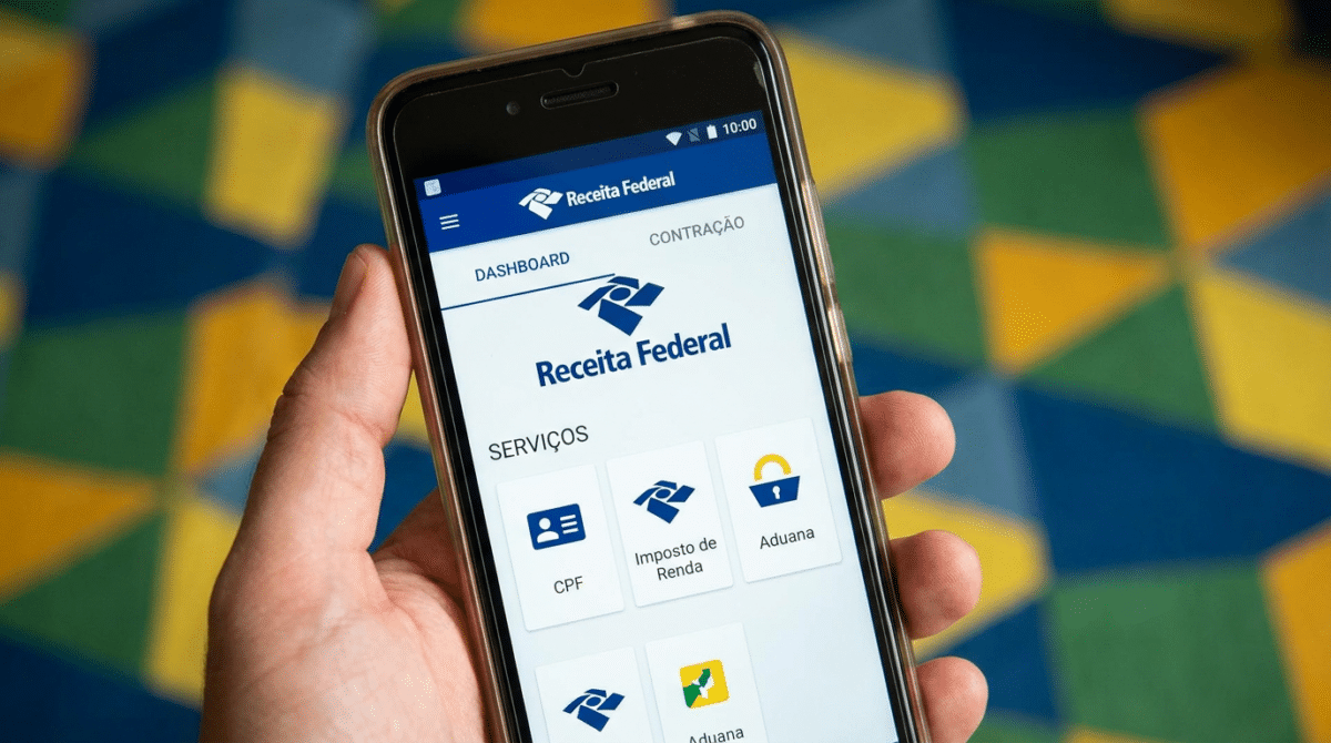 Mão segura celular com o aplicativo da Receita Federal aberto na tela inicial de serviços.