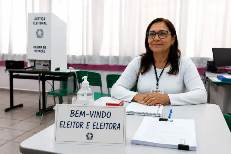 Mesária voluntária em seção eleitoral aguardando eleitores para atendimento nas eleições de 2026