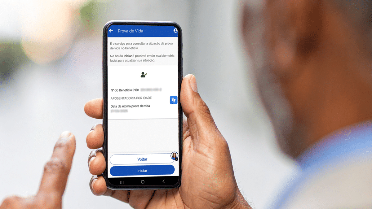 Homem idoso segura celular com a tela do serviço Prova de Vida do aplicativo Meu INSS aberta exibindo dados do benefício