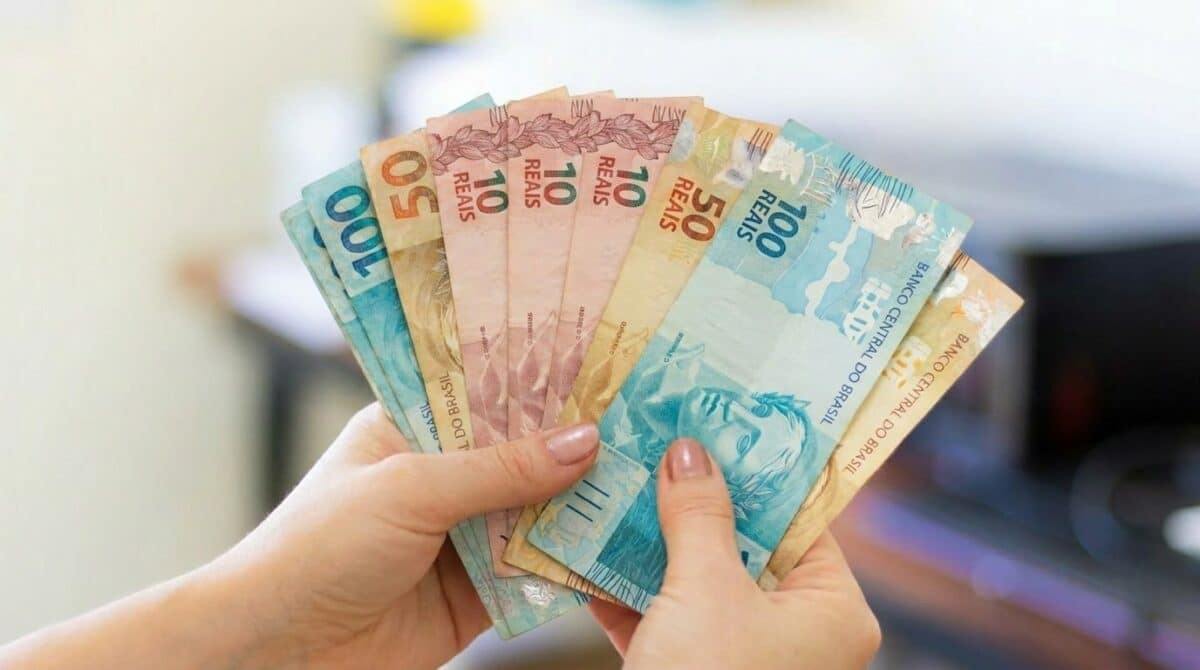 Mãos seguram em leque cédulas de dez, cinquenta e cem reais.