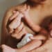 Mãe segura o bebê recém-nascido nos braços, com a mãozinha da criança apoiada em sua mão.