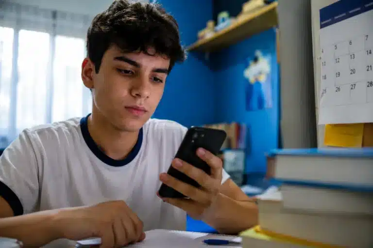 Estudante consulta o celular enquanto estuda, representando a busca de informações sobre o valor e o prazo de pagamento da taxa do Enem 2026.