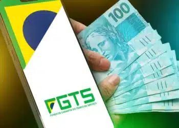 Smartphone exibindo logotipo do FGTS ao lado de cédulas de cem reais sobre fundo verde e amarelo com bandeira do Brasil