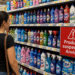 Consumidora observa prateleira de supermercado com produtos Ypê e placa vermelha de alerta "Produtos suspensos Anvisa"