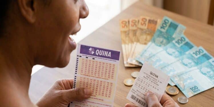 Mulher segura volante e recibo da Quina sobre mesa com notas de 50 e 100 reais e moedas