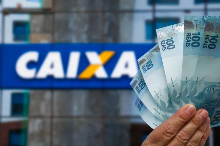 Mão segura cédulas de R$ 100 em frente à fachada de uma agência da Caixa Econômica Federal