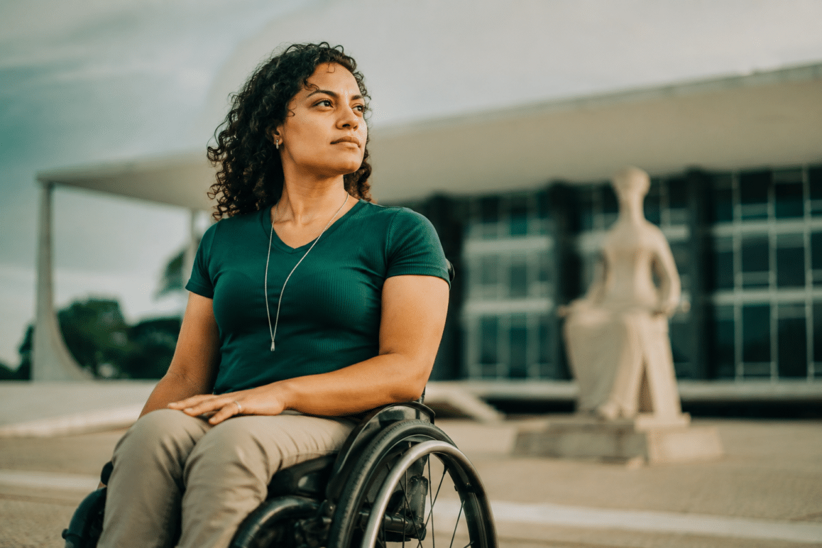 Mulher de cabelos cacheados em cadeira de rodas diante da estátua A Justiça, no STF, Brasília.