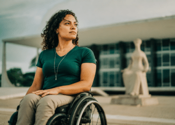 Mulher de cabelos cacheados em cadeira de rodas diante da estátua A Justiça, no STF, Brasília.
