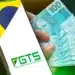 Celular exibindo o aplicativo do FGTS ao lado de cédulas de R$ 100 em mão, em referência ao saque digital pela modalidade Saque-Aniversário
