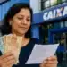 Mulher brasileira segurando cédulas de R$ 50 e R$ 100 e conferindo documento em frente à Caixa, representando o saque de R$ 6.220.