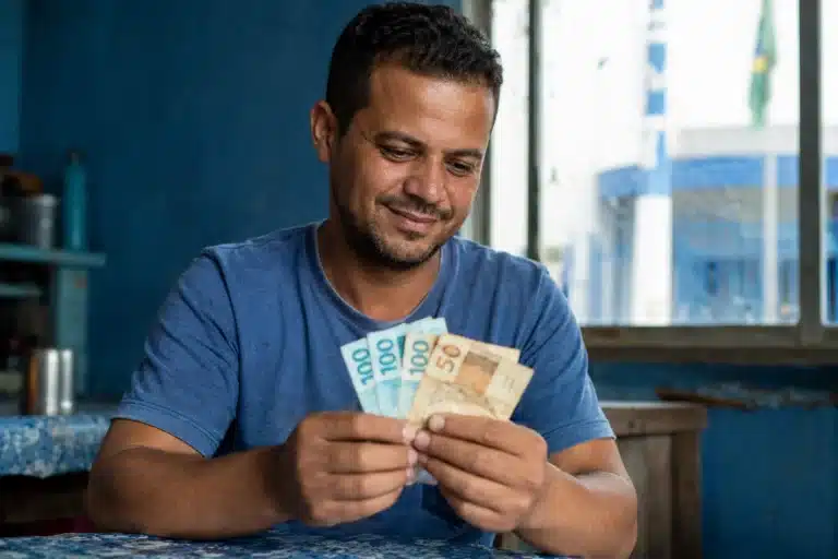 Homem segurando cédulas em ambiente doméstico, ilustrando o saque do FGTS de R$ 6.220 liberado para solicitação a partir de 27 de maio.