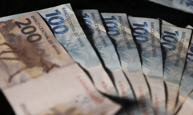 Cédulas de duzentos e cem reais dispostas em formato de leque sobre fundo escuro