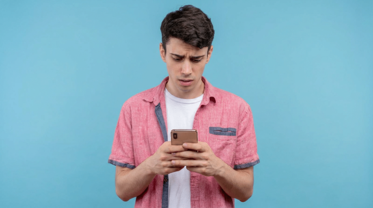 Jovem confuso olhando celular com expressão preocupada.