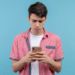 Jovem confuso olhando celular com expressão preocupada.