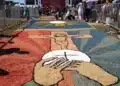 Tapete colorido de Corpus Christi com símbolos religiosos sendo confeccionado por participantes em procissão.