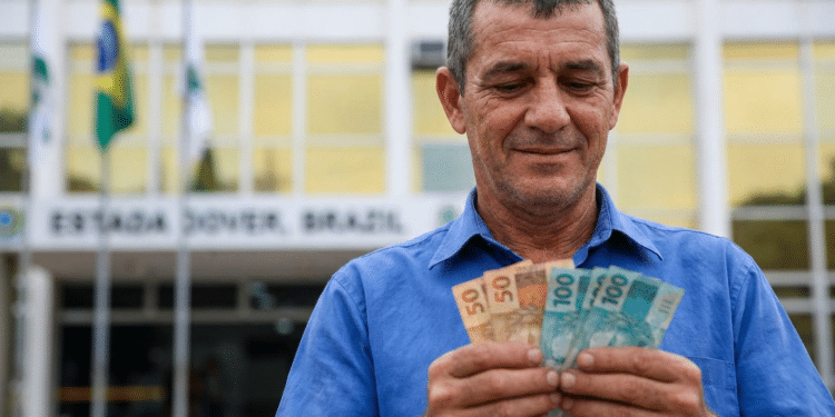 Servidor público sorri ao contar cédulas de 50 e 100 reais em frente a prédio governamental com bandeiras