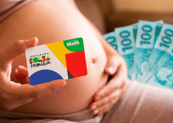 Gestante segura cartão do Programa Bolsa Família com logotipo colorido enquanto mostra notas de R$ 100 ao fundo