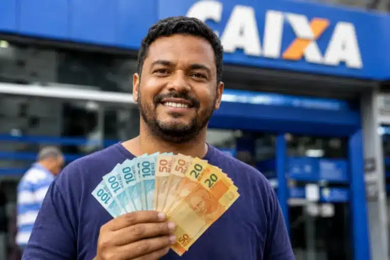 Homem brasileiro sorridente segurando cédulas de reais em frente à agência da Caixa Econômica Federal, ilustrando o saque de R$ 6.220 da Caixa.