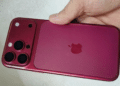 Mão segurando iPhone na cor vinho/burgundy com módulo de câmera tripla e logo da Apple visível.