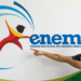 Jovem candidato sorri ao apontar para a logomarca do Exame Nacional do Ensino Médio em painel ilustrado