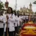 iéis participando de uma procissão de Corpus Christi em rua brasileira, com tapetes coloridos de serragem e flores, representando o feriado de Corpus Christi.