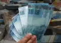 Mão segurando notas de real, simbolizando o saque de R$ 6.220 disponível para solicitação por meio do aplicativo FGTS.