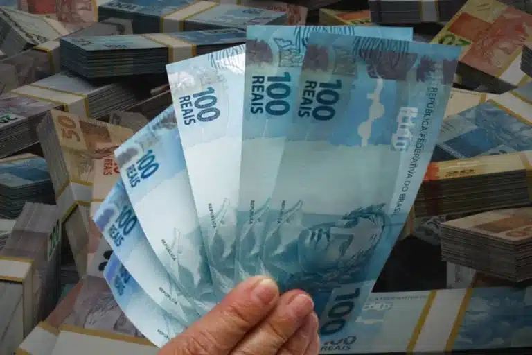 Mão segurando notas de real, simbolizando o saque de R$ 6.220 disponível para solicitação por meio do aplicativo FGTS.