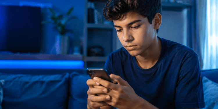 Jovem de cabelos escuros e camiseta azul marinho usa celular em ambiente noturno com iluminação LED azul.