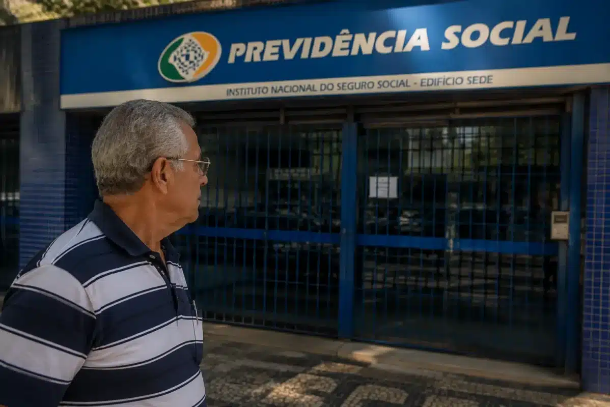Idoso observando agência do INSS fechada, representando a suspensão de pagamentos de benefícios nesta quinta-feira, 4 de junho.