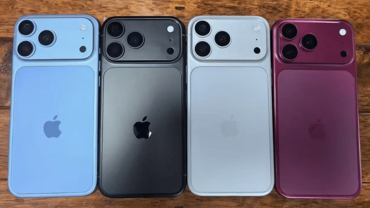 Quatro iPhones sobre mesa de madeira exibindo cores azul, preto, branco e rosa com sistema de câmeras triplas.